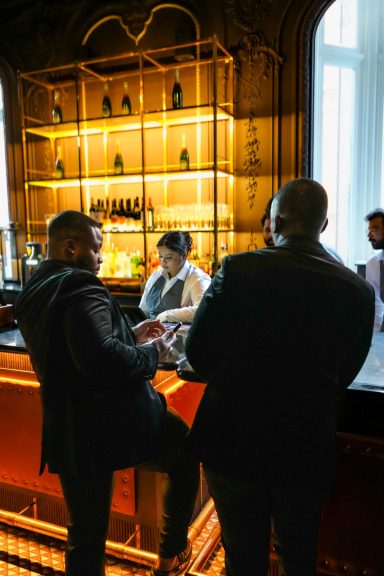 Two patrons at a stylish bar, engaging with a bartender behind a well-lit counter.